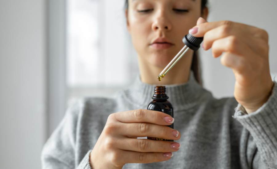Personne déposant une pipette d’huile de CBD sous la langue, démontrant la méthode de consommation sublinguale pour un effet relaxant rapide et naturel contre l’épuisement professionnel.