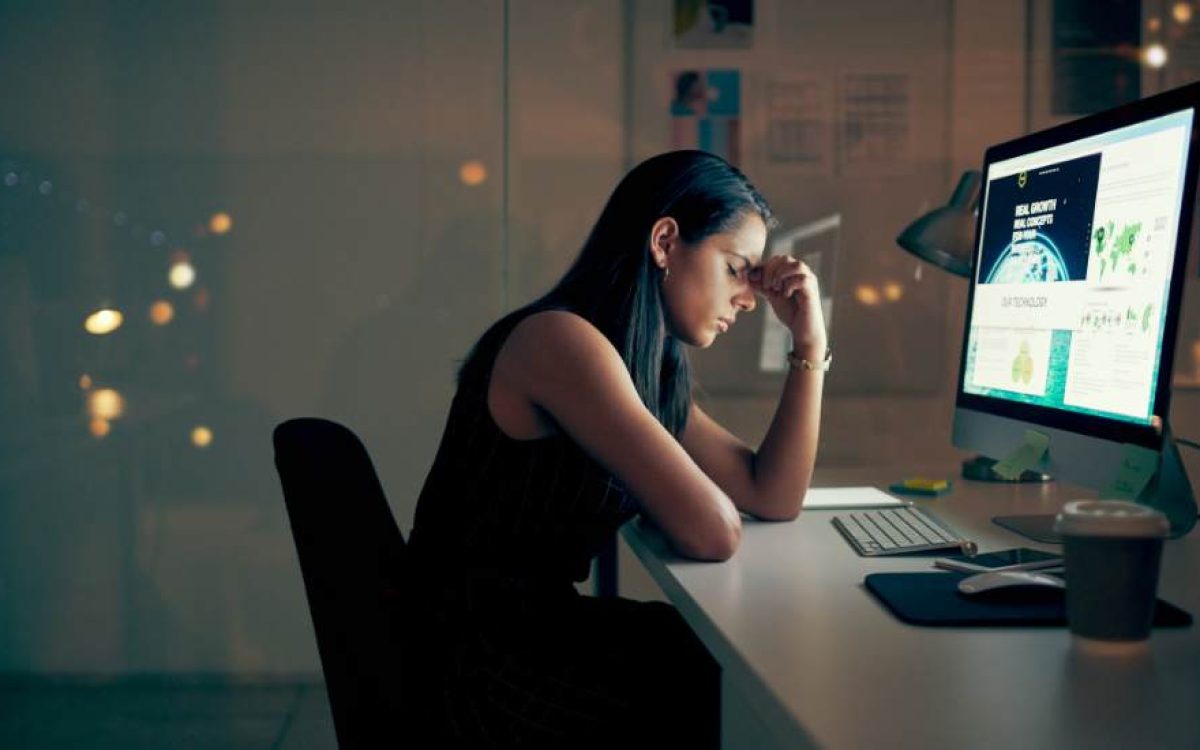 Employée fatiguée devant son ordinateur en soirée, symbole du stress professionnel et du burn-out, contexte de l’utilisation du CBD pour apaiser l’épuisement mental.